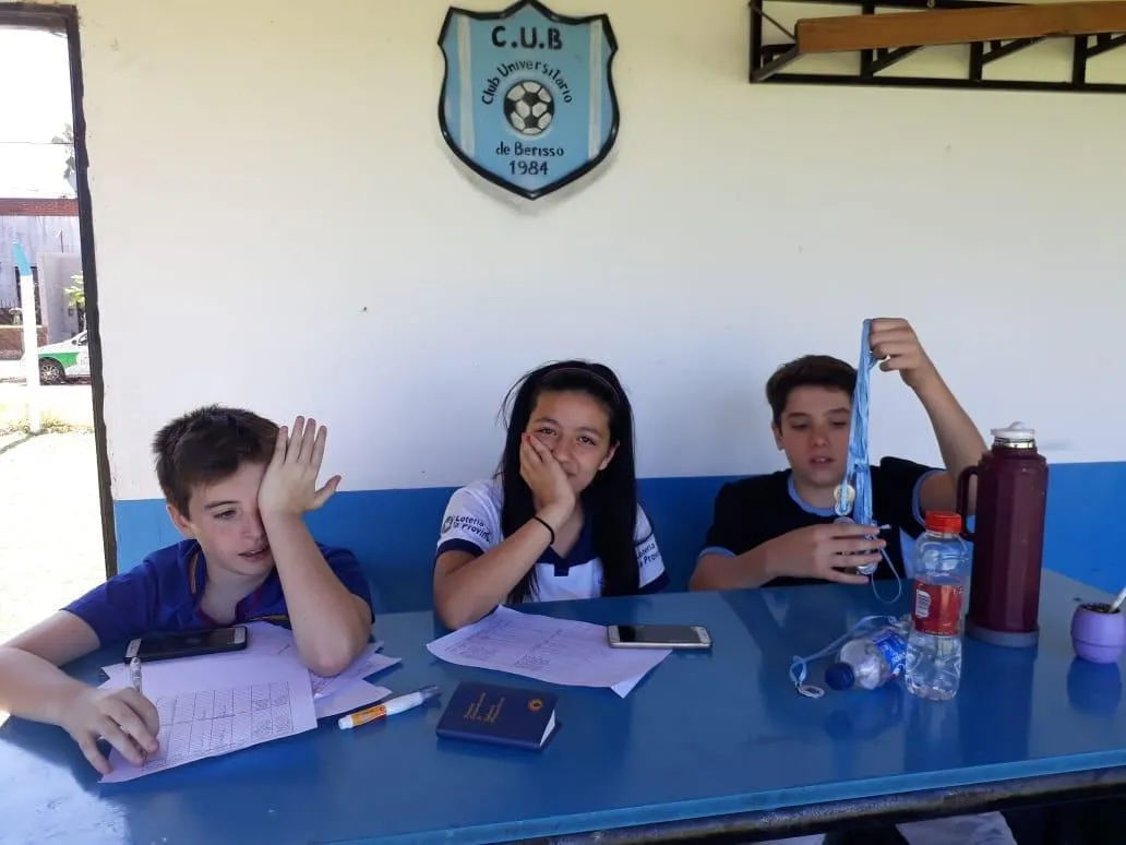 Tres chicos estudiando en una mesa del club, con el escudo en la pared