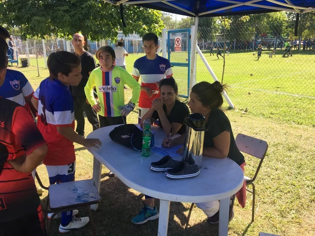 Chicos y grandes bajo un gazebo al costado de la cancha durante una jornada en el club